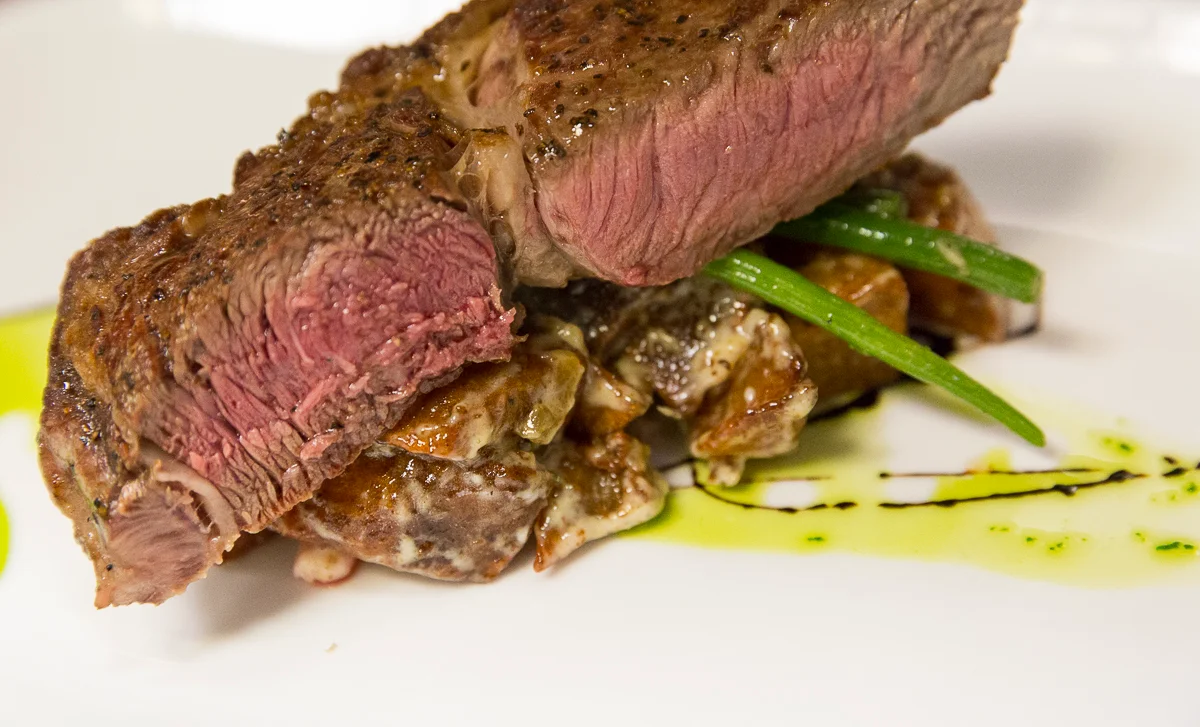 Sliced steak served over vegetables on a white plate.