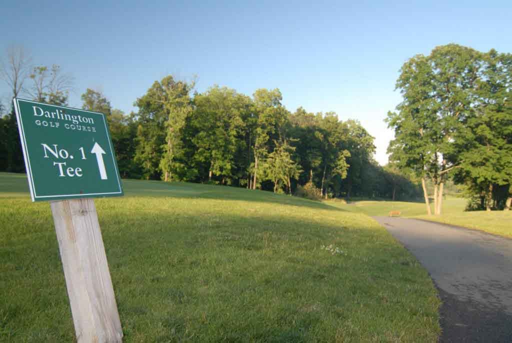 Darlington Golf Course’s first-tee sign beside the fairway and a paved path.