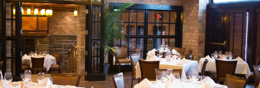 Dining room at Roots Steakhouse in Ridgewood, with wood trim and white tablecloths.