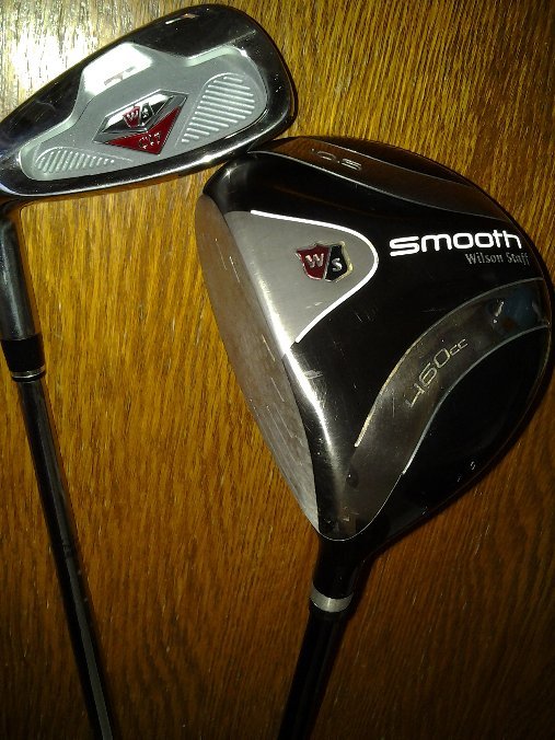 A Wilson wedge and driver resting against a wood surface.