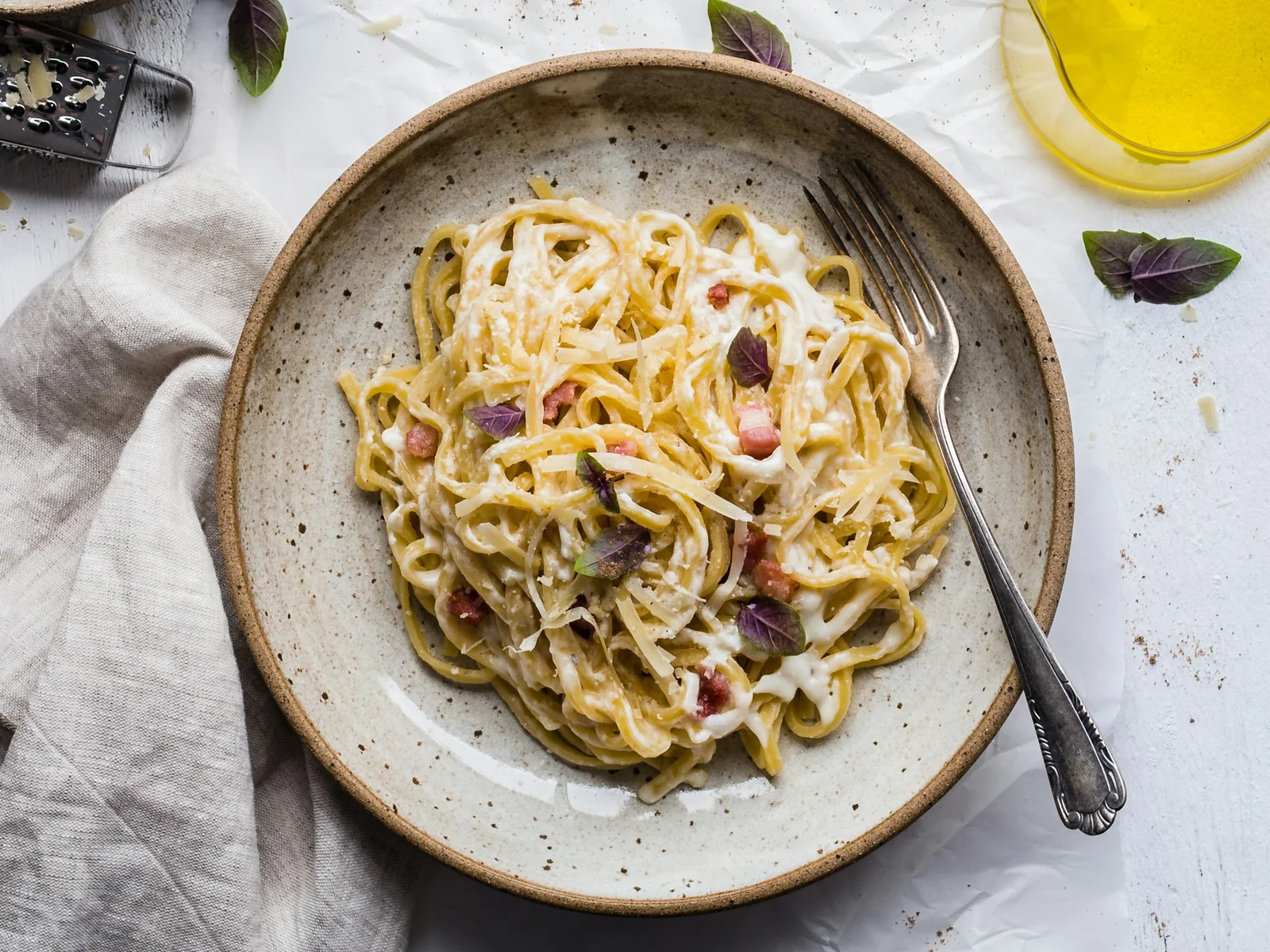 Creamy pasta on a ceramic plate with a fork, herbs and olive oil on the table.